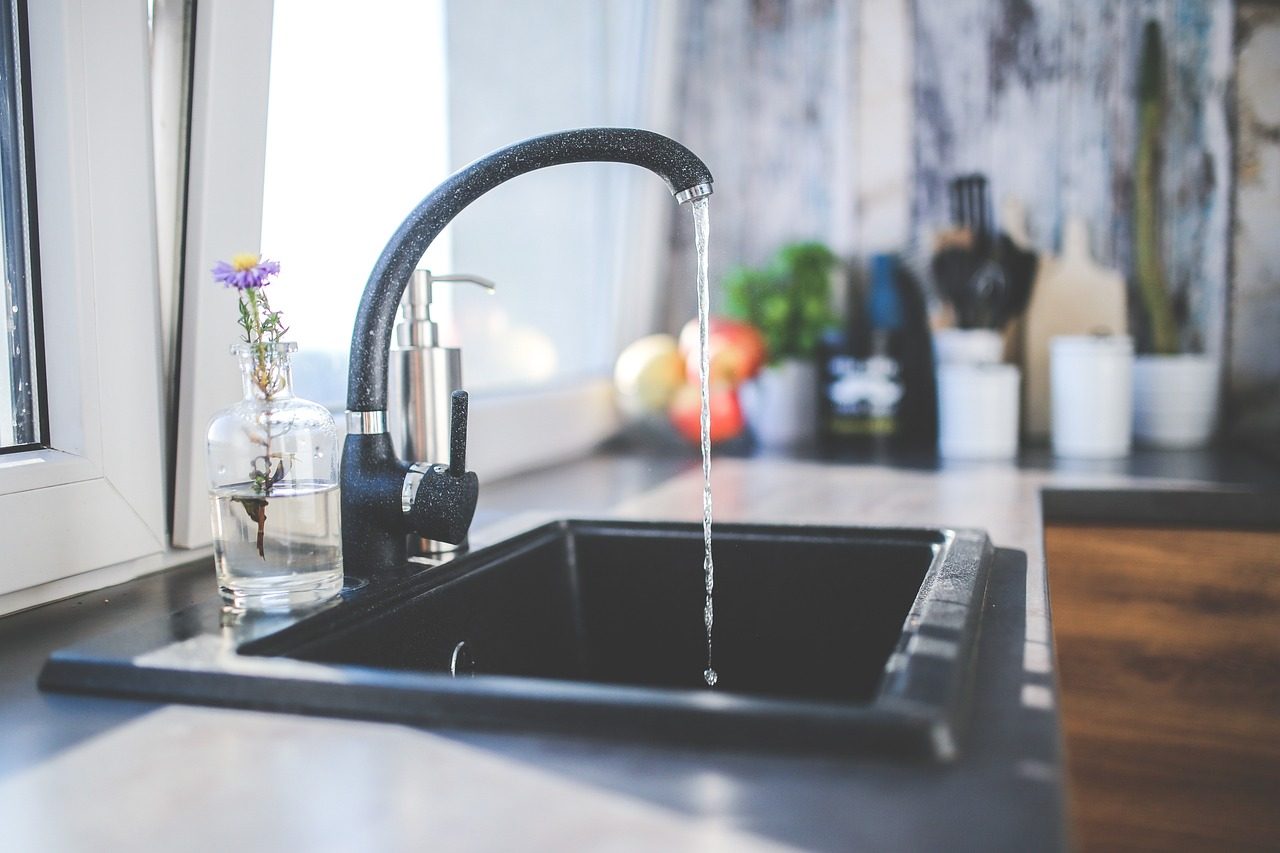 Personne buvant un verre d'eau debout dans une cuisine, lumière naturelle